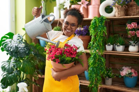 Téléchargez les photos : Afro-américaine femme fleuriste arrosage plante à fleur boutique - en image libre de droit