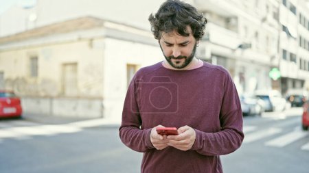 Photo for Young hispanic man using smartphone with serious expression at street - Royalty Free Image