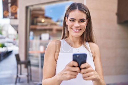 Téléchargez les photos : Jeune belle femme hispanique souriant confiant en utilisant smartphone à la terrasse du café - en image libre de droit