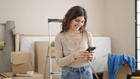Photo for Young beautiful hispanic woman using smartphone standing at new home - Royalty Free Image