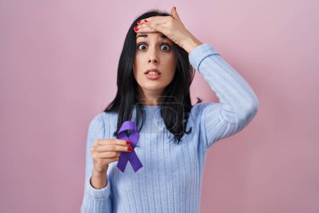 Foto de Mujer hispana sosteniendo la conciencia de la cinta púrpura estresada y frustrada con la mano en la cabeza, cara sorprendida y enojada - Imagen libre de derechos