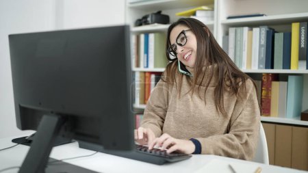Téléchargez les photos : Belle étudiante hispanique utilisant l'ordinateur parlant sur smartphone à l'université de la bibliothèque - en image libre de droit