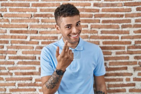 Téléchargez les photos : Jeune homme brésilien debout au-dessus du mur de briques signe venir ici geste avec la main invitant accueillant heureux et souriant - en image libre de droit
