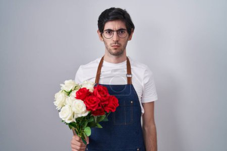 Foto de Joven hombre hispano sosteniendo ramo de rosas blancas y rojas escéptico y nervioso, frunciendo el ceño molesto debido a un problema. persona negativa. - Imagen libre de derechos