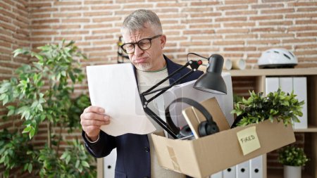 Foto de Hombre de pelo gris de mediana edad trabajador de negocios que lee el documento de despido en la oficina - Imagen libre de derechos