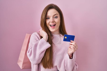 Photo for Young caucasian woman holding shopping bag and credit card celebrating crazy and amazed for success with open eyes screaming excited. - Royalty Free Image