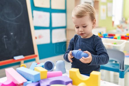 Foto de Adorable niño rubio jugando con bloques de geometría de pie en el jardín de infantes - Imagen libre de derechos