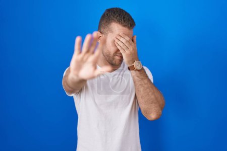 Photo for Young caucasian man standing over blue background covering eyes with hands and doing stop gesture with sad and fear expression. embarrassed and negative concept. - Royalty Free Image