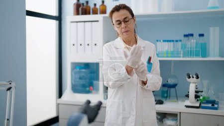 Foto de Mujer hispana de mediana edad con uniforme científico y guantes en el laboratorio - Imagen libre de derechos