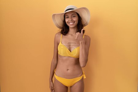 Photo for Young hispanic woman wearing bikini and summer hat doing happy thumbs up gesture with hand. approving expression looking at the camera showing success. - Royalty Free Image