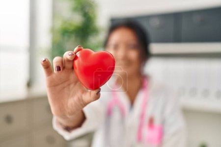 Photo for Young chinese woman wearing doctor uniform holding heart at clinic - Royalty Free Image