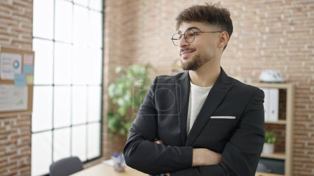 Téléchargez les photos : Jeune homme arabe homme d'affaires souriant confiant debout avec les bras croisés geste au bureau - en image libre de droit