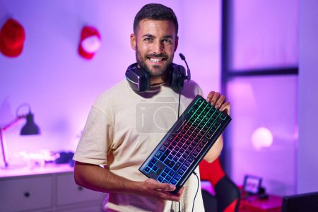 Photo for Young hispanic man streamer smiling confident holding keyboard computer at gaming room - Royalty Free Image