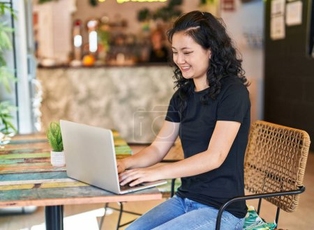 Foto de Young chinese woman using laptop sitting on table at restaurant - Imagen libre de derechos