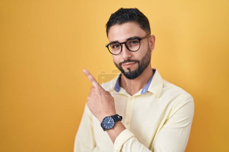 Photo for Hispanic young man wearing business clothes and glasses pointing with hand finger to the side showing advertisement, serious and calm face - Royalty Free Image