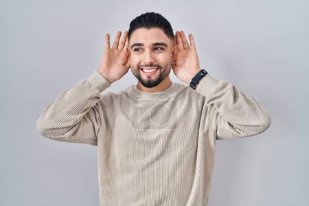 Photo for Young handsome man standing over isolated background trying to hear both hands on ear gesture, curious for gossip. hearing problem, deaf - Royalty Free Image