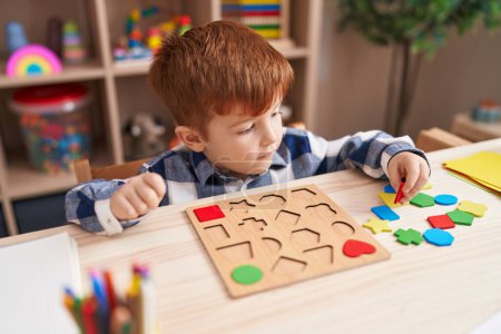 Foto de Adorable niño jugando con las matemáticas juego de puzzle sentado en la mesa en el aula - Imagen libre de derechos