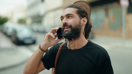 Foto de Joven músico hispano hablando en smartphone sosteniendo estuche de guitarra en la calle - Imagen libre de derechos