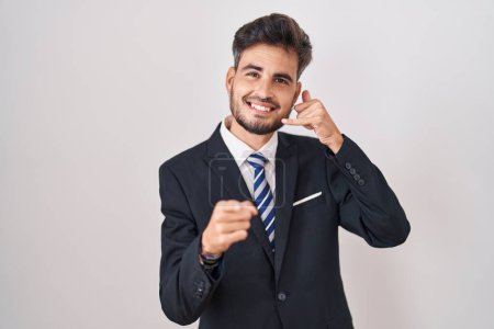 Téléchargez les photos : Jeune homme hispanique avec des tatouages portant un costume d'affaires et une cravate souriant faisant parler au téléphone et vous pointant du doigt. Appelle-moi. - en image libre de droit