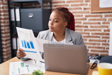 Téléchargez les photos : Femme afro-américaine travailleur d'affaires en utilisant un ordinateur portable document de lecture au bureau - en image libre de droit