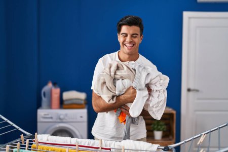 Foto de Hombre hispano colgando ropa en el tendedero sonriendo y riendo en voz alta porque gracioso chiste loco. - Imagen libre de derechos