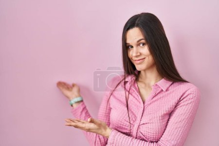 Foto de Mujer hispana joven de pie sobre fondo rosa invitando a entrar sonriendo natural con la mano abierta - Imagen libre de derechos