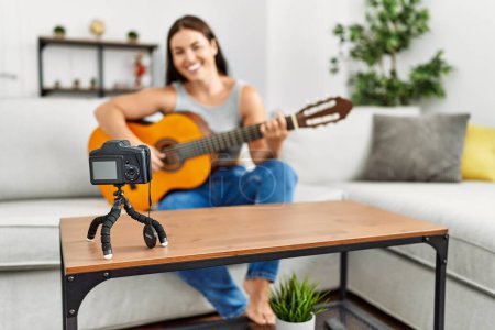 Photo for Young beautiful hispanic woman having playing classical guitar recording video at home - Royalty Free Image