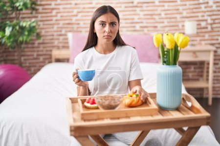 Photo for Young hispanic woman eating pastries for breakfast sitting on the bed skeptic and nervous, frowning upset because of problem. negative person. - Royalty Free Image