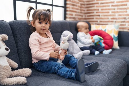 Photo for Adorable boy and girl sitting on sofa playing with dolls at home - Royalty Free Image