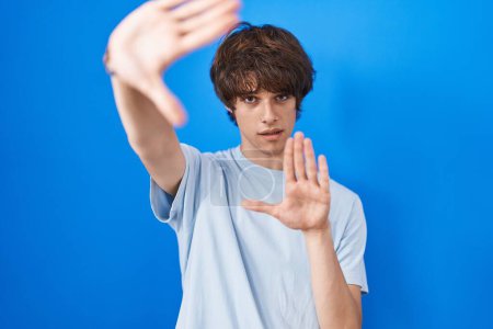Photo for Hispanic young man standing over blue background doing frame using hands palms and fingers, camera perspective - Royalty Free Image