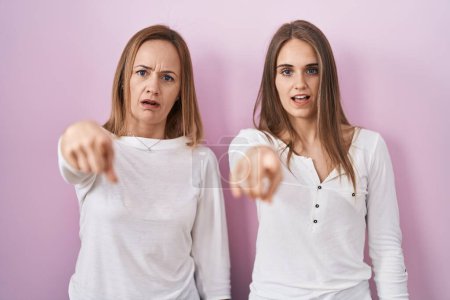 Photo for Middle age mother and young daughter standing over pink background pointing displeased and frustrated to the camera, angry and furious with you - Royalty Free Image
