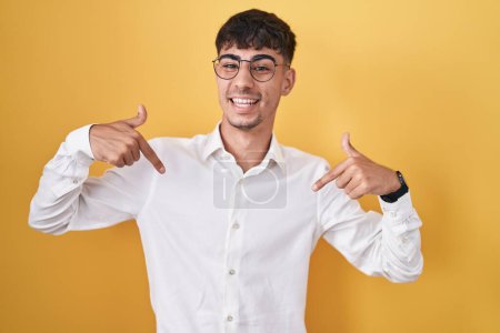 Photo for Young hispanic man standing over yellow background looking confident with smile on face, pointing oneself with fingers proud and happy. - Royalty Free Image