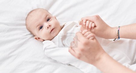Foto de Adorable bebé caucásico acostado en la cama sosteniendo las manos de la madre en el dormitorio - Imagen libre de derechos