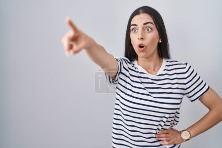 Photo for Young brunette woman wearing striped t shirt pointing with finger surprised ahead, open mouth amazed expression, something on the front - Royalty Free Image