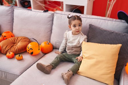 Foto de Adorable chica hispana teniendo fiesta de halloween sentada en el sofá en casa - Imagen libre de derechos