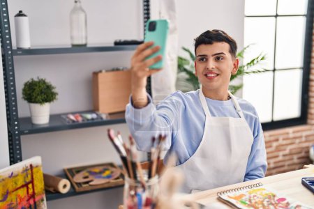 Téléchargez les photos : Jeune homme non binaire artiste souriant confiant faire selfie par smartphone au studio d'art - en image libre de droit