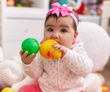 Photo for Adorable hispanic baby sitting on floor sucking duck toy at home - Royalty Free Image