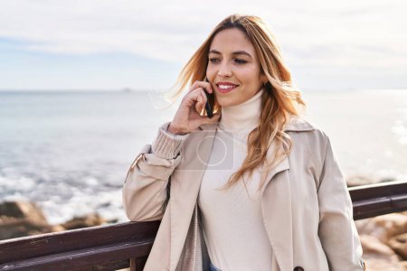 Photo for Young blonde woman smiling confident talking on smartphone at seaside - Royalty Free Image