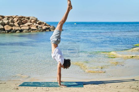 Téléchargez les photos : Young hispanic man training handstand yoga pose at beach - en image libre de droit