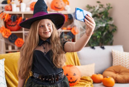 Foto de Adorable chica rubia con traje de bruja hacer selfie por teléfono inteligente en casa - Imagen libre de derechos