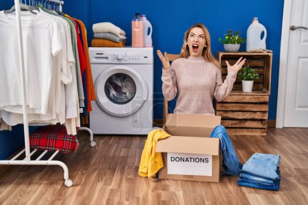 Photo for Hispanic woman putting clothes in donation box crazy and mad shouting and yelling with aggressive expression and arms raised. frustration concept. - Royalty Free Image