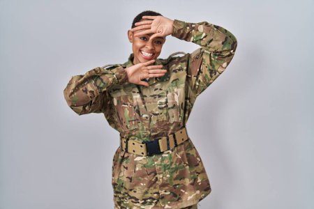 Foto de Hermosa mujer afroamericana vistiendo camuflaje uniforme del ejército sonriendo alegre jugando a echar un vistazo a un boo con las manos mostrando la cara. sorprendido y salido - Imagen libre de derechos