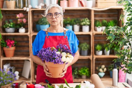 Photo for Middle age woman with grey hair working at florist shop holding plant skeptic and nervous, frowning upset because of problem. negative person. - Royalty Free Image