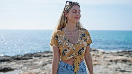 Téléchargez les photos : Jeune femme blonde respirant les yeux fermés au bord de la mer - en image libre de droit