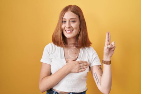 Photo for Young redhead woman standing over yellow background smiling swearing with hand on chest and fingers up, making a loyalty promise oath - Royalty Free Image