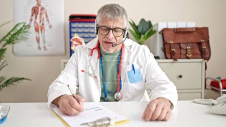 Foto de Médico de pelo gris de mediana edad que tiene consulta médica en línea en la clínica - Imagen libre de derechos