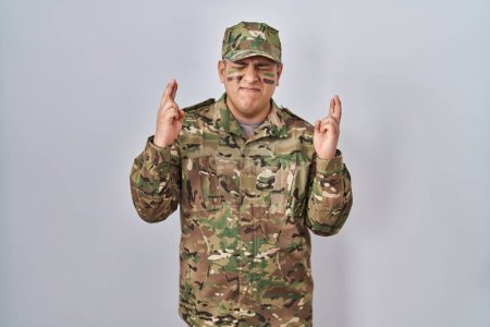 Photo for Hispanic young man wearing camouflage army uniform gesturing finger crossed smiling with hope and eyes closed. luck and superstitious concept. - Royalty Free Image