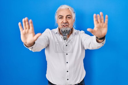 Téléchargez les photos : Homme du Moyen Age avec les cheveux gris debout sur fond bleu faisant geste d'arrêt avec les mains paumes de la main, expression de colère et de frustration - en image libre de droit
