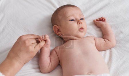 Photo for Adorable caucasian baby lying on bed holding mother finger at bedroom - Royalty Free Image