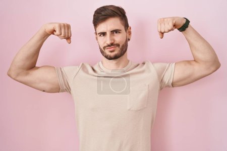 Téléchargez les photos : Homme hispanique avec barbe debout sur fond rose montrant les muscles des bras souriant fier. concept de fitness. - en image libre de droit